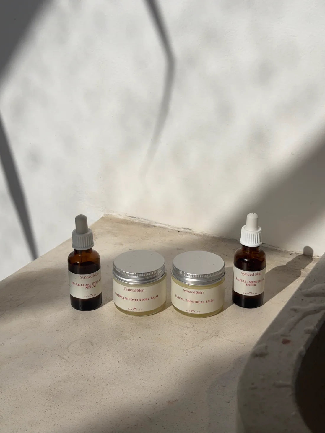 Full Size Synced Skin Starter Kit with two 1 oz face serums and two 2 oz tallow balms on a sunlit ledge