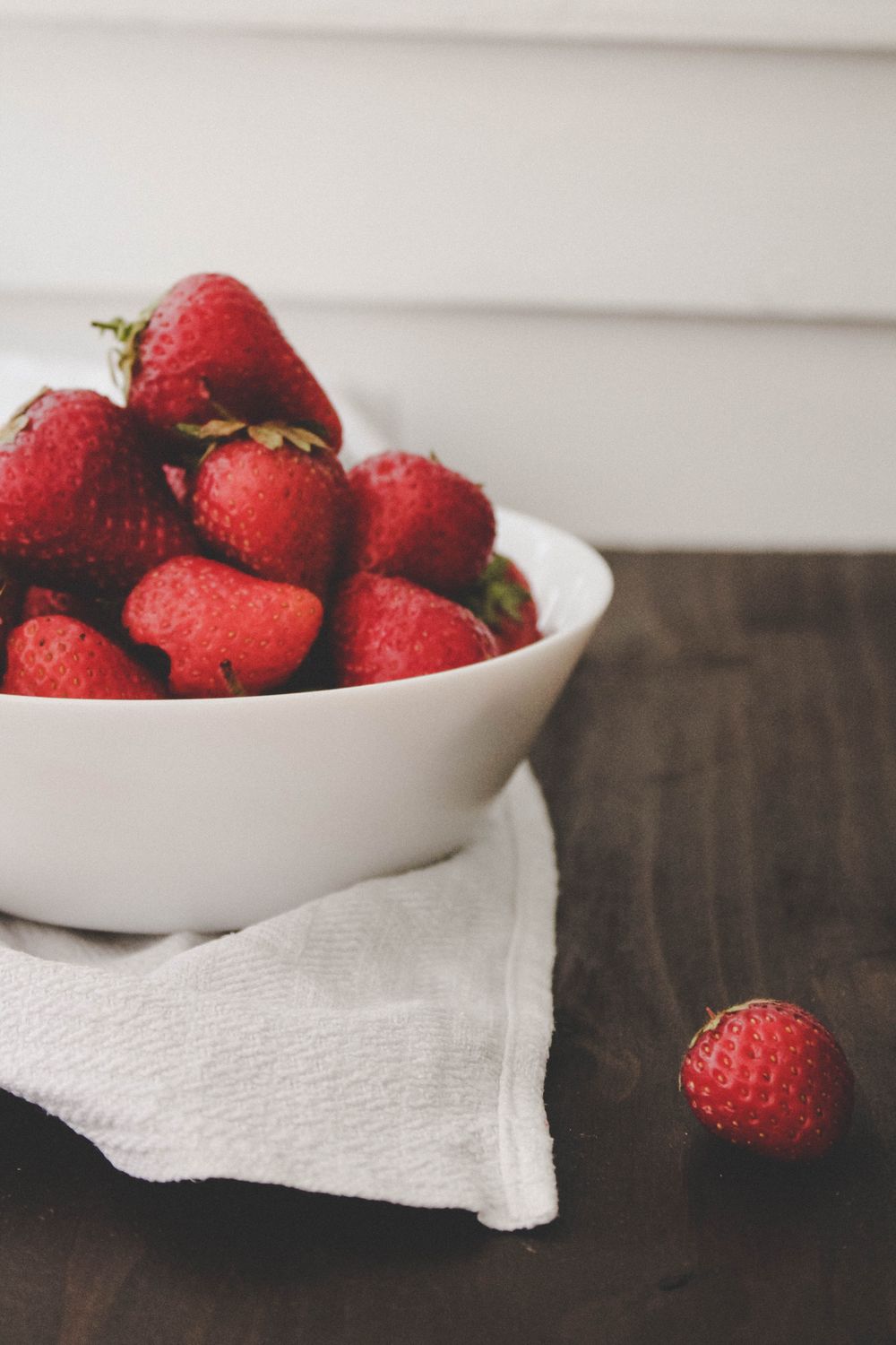 Fresh strawberries in a white bowl on a linen-covered wooden table.