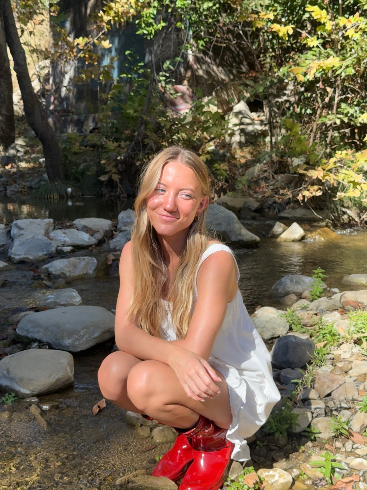 Madi sitting beside a shaded creek in red boots.